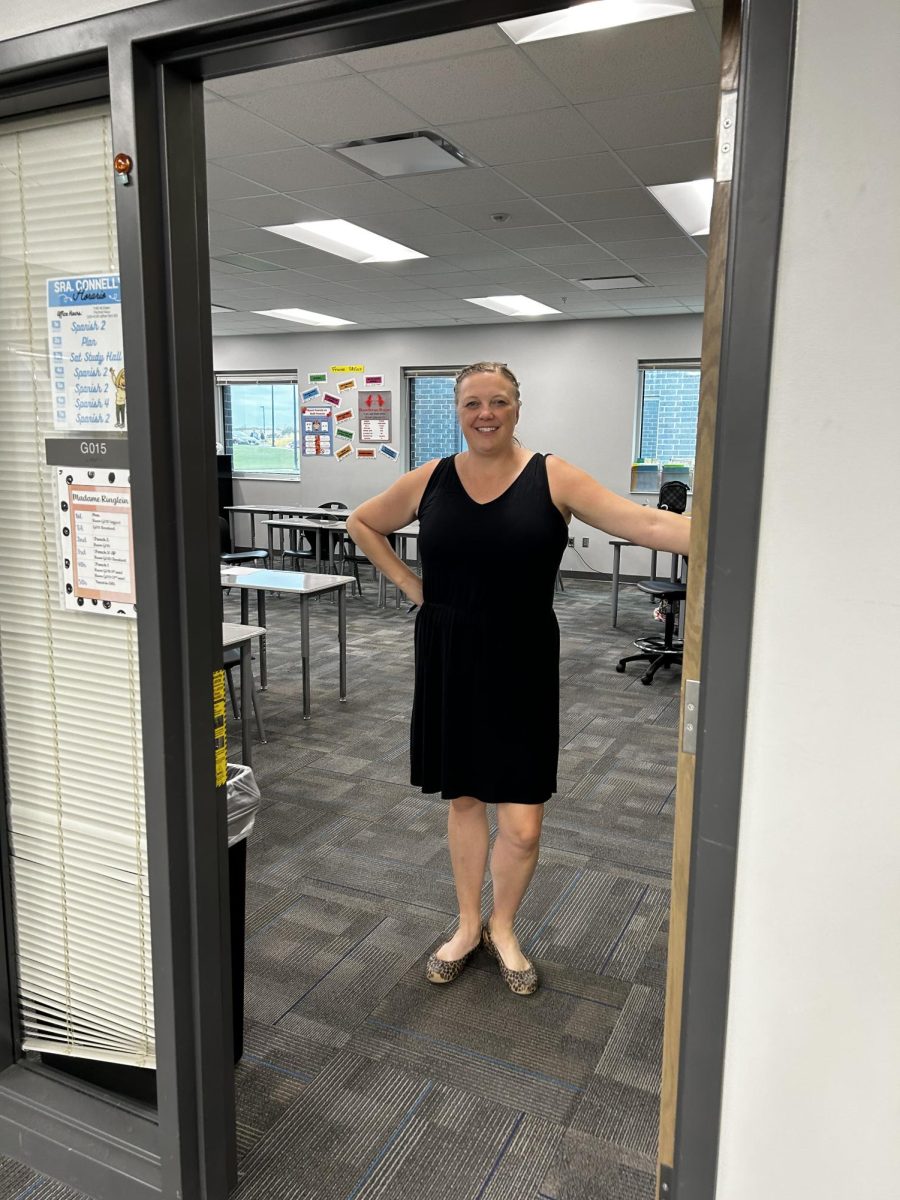 Mrs. Connelly standing in front of her Spanish II and III classroom, located in G015. Inside is a vast amount of decorations and vibrant colors.