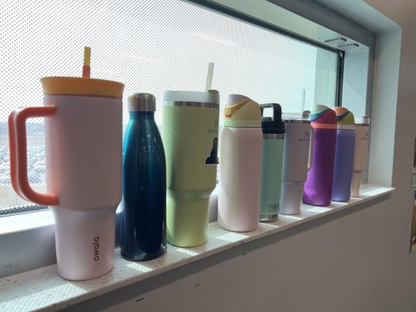 A line of various student water bottles in just one classroom. The brands of these range from Owalas to Stanley Cups and more. 