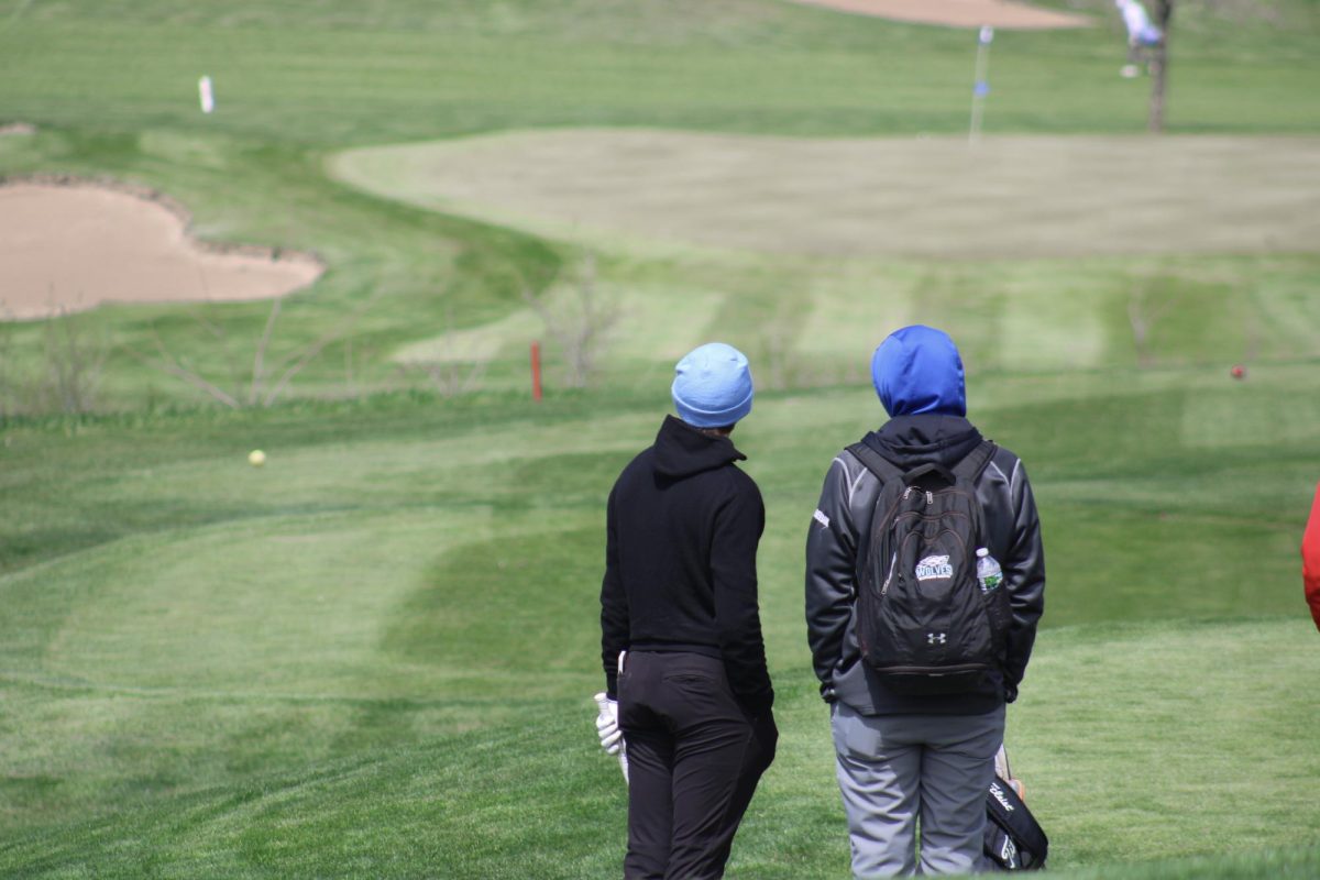 Cole Dryak (12) discusses with his coach his plan for the par three at River Wilds. He lands his shot on the back left of the green, despite he heavy wind at the Blair invite on April 19, 2024.