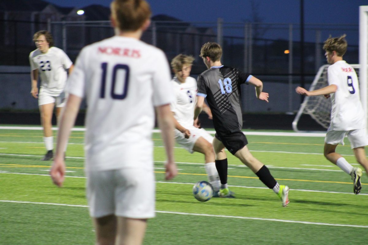 Junior Noah Burgland (18) attempting to pass the ball with two opponents trying to take possession. Burgland made the pass successfully and contributed to the game on Tuesday, April the 23rd.