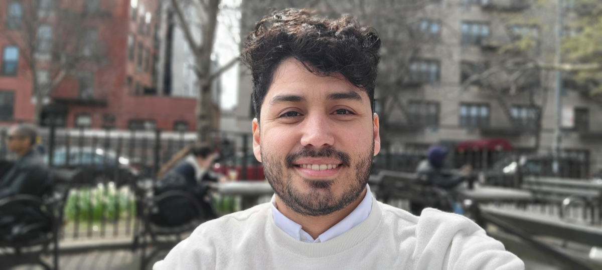 Spanish teacher Kenny Navarro smiles in front of buildings in a foreign country.