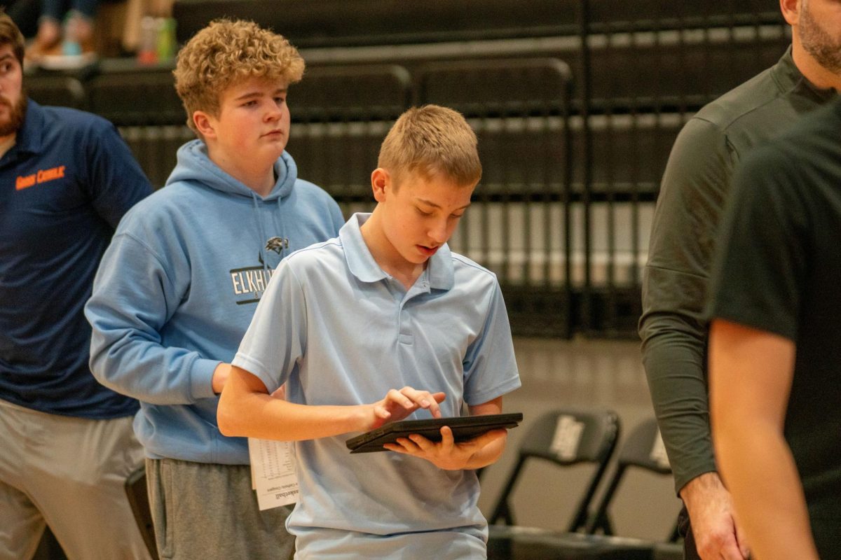 Team manager Adam Pospisil looks down at his iPad to finish recording the Wolves basketball team's first half stats against the Cougars of Gross Catholic. These stats helped the team make a game plan for the second half and understand how to attack in a different way than the first.
