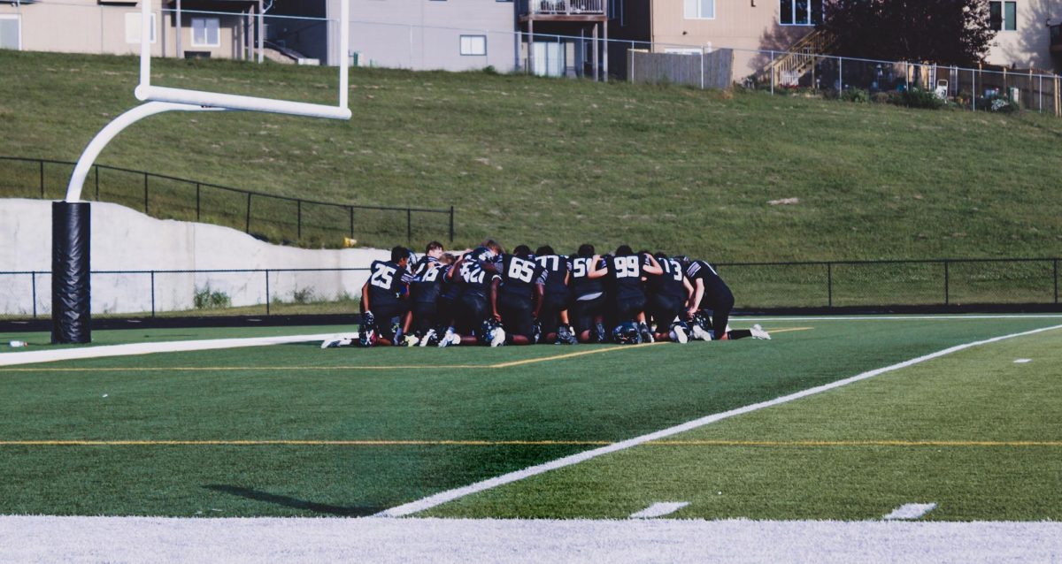 The freshman football team is crouched in a huddle before the game. This is their first home game of the season and they kneeled together to talk.