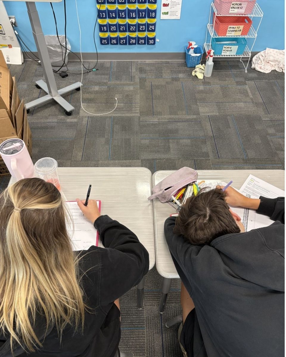 Two students in class working. One is clearly organized doing their work, the other has their work all over the place. Graphic By Hannah Skudlarek